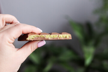 A hand holding a sleek piece of trendy Dubai chocolate with a vibrant green pistachio filling....