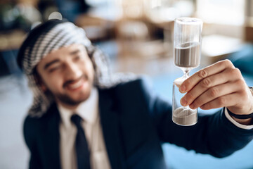 Arab businessman with hourglass at table at hotel room.