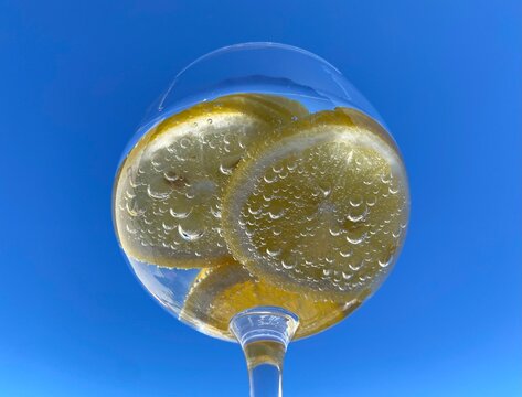 Close-up of glass of sparkling citrus drink with lemon slices against a bright blue sky. Tiny bubbles cling to the fruit, enhancing the fresh and refreshing feel. Summer, hydration, healthy beverage