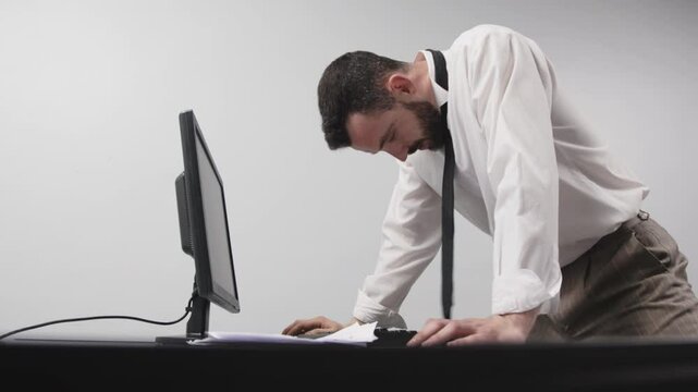 A businessman in aggression loses his temper in a fit of rage. An enraged office worker smashes a computer monitor with his keyboard, throws things off his desk and screams. Financial crisis or layoff