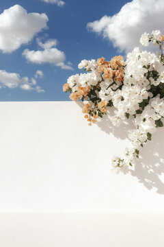 Fototapeta Blossoming flowers cascade over a pristine white wall against a backdrop of a clear blue sky with clouds.