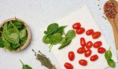 Wooden bowl with spinach, cherry tomatoes, wooden spoon with spices, and a bunch of thyme