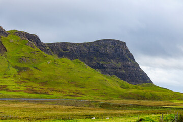 Obraz premium Neist Point at sunset is a breathtaking sight—its lighthouse stands against dramatic cliffs, with waves crashing below. A rainbow arches over the ocean, painting the rugged Isle of Skye magical light