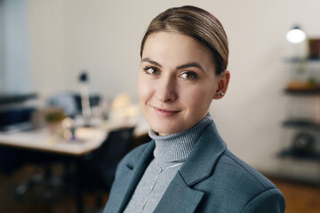 Portrait of pretty young businesswoman in suit looking at camera while working in office