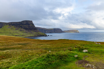 Neist Point at sunset is a breathtaking sight—its lighthouse stands against dramatic cliffs, with waves crashing below. A rainbow arches over the ocean, painting the rugged Isle of Skye magical light