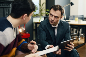 Businessman using his digital tablet and talking to job candidate at meeting