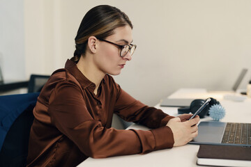 Businesswoman sitting at her workplace in office and texting message on her mobile phone