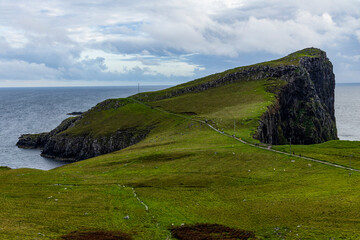 Neist Point at sunset is a breathtaking sight—its lighthouse stands against dramatic cliffs, with waves crashing below. A rainbow arches over the ocean, painting the rugged Isle of Skye magical light