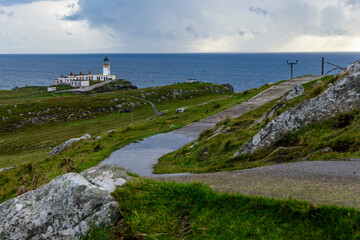 Fototapeta na wymiar Neist Point at sunset is a breathtaking sight—its lighthouse stands against dramatic cliffs, with waves crashing below. A rainbow arches over the ocean, painting the rugged Isle of Skye magical light