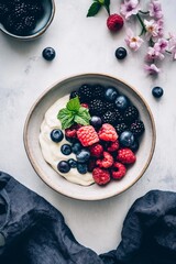 Yogurt bowl with mixed berries and mint on white surface with flowers and extra berries