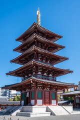 Fototapeta premium Shitenno-ji Gojunoto - A five-story pagoda stands tall against a clear blue sky in Osaka, Japan. Its intricate red wooden structure and golden details showcase traditional Japanese craftsmanship.