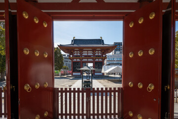 Open red temple gates reveal a traditional Japanese pagoda gate (Grand West Gate) and courtyard at...