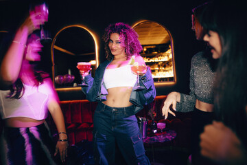 Group of young women partying in a nightclub with cocktails and vibrant lights