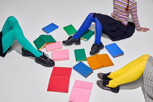 Colorful legs and feet amidst scattered open and closed books suggest collaborative study and vibrant atmosphere of knowledge day. Education, library, homework, childhood concept.