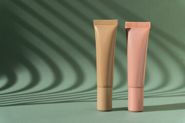 Natural foundation cream tubes mockup. Brown and pink lotion containers on green background with Light on wall.