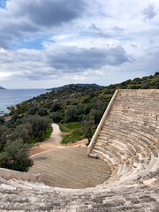 Ancient Roman Amphitheater In Kaş, Turkey, Overlooking The Sea During Spring, Surrounded By Green Hills And Cloudy Sky, Concept Of Cultural Heritage, Travel, History, And Architecture