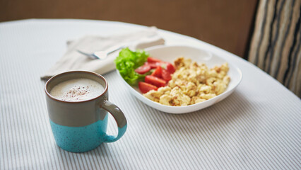 Breakfast table. Cup of coffee and plate with scrambled eggs and vegetables on the table
