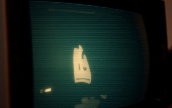 A simplistic white figure with a face is displayed on an old CRT monitor screen, set in a dimly lit room. The image evokes a retro digital aesthetic.