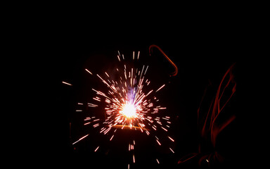 A burst of bright sparks emanates from a welding point against a stark black backdrop, illuminating the immediate area with intense light and highlighting the metalworking process.