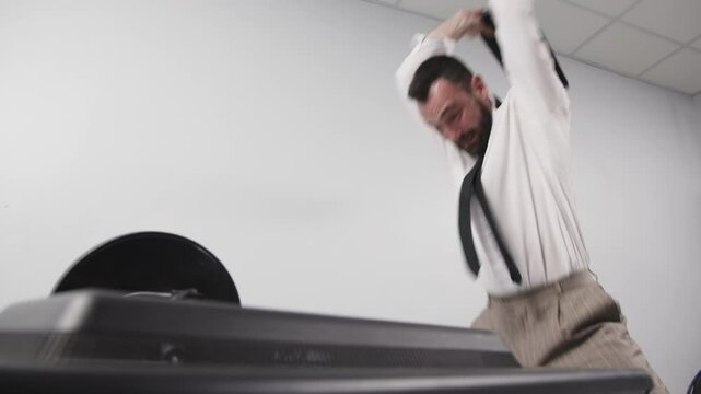 A businessman in aggression loses his temper in a fit of rage. An enraged office worker smashes a computer monitor with his keyboard, throws things off his desk and screams. Financial crisis or layoff