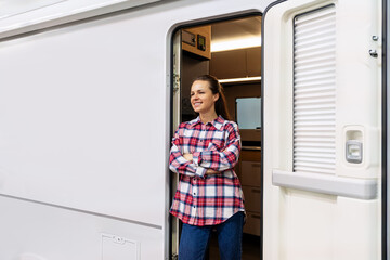 Confident female RV owner standing at motorhome entrance with crossed arms and smiling