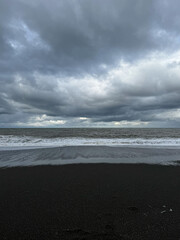Ocean waves washing onto a black sand beach under stormy clouds