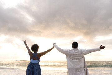African couple raising their arms to the sky on a beach at dusk