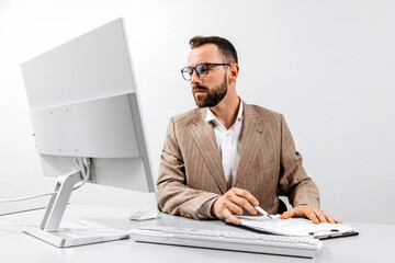 Fototapeta premium Tired, focused business man working at a computer in a bright office. The man looks frustrated while working. The concept of stress, frustration and burnout in the workplace.