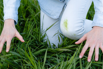 Dirty grass stains in clothes during summertime activities in outdoors. A person sits in lush green...