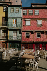 Vibrant facade of traditional Portuguese buildings decorated with colorful azulejo tiles in red and turquoise, overlooking an empty outdoor cafe terrace in Porto, Portugal. Charming urban scene reflec