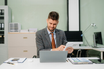 Confident businessman working on finance analysis with a tablet and laptop at office desk