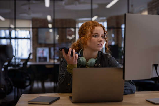 Young Woman Using Phone While Working late on Computer 
