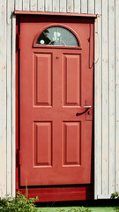 Close-Up of a Red Wooden Door with Ornate Glass Window and a Light Plank Wall