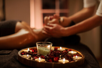 Aroma therapy in spa. Focus on wooden tray with candles and salt while young woman having facial massage on background, side view, closeup