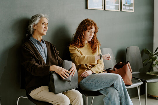 Two women sitting in waiting area of office, one with folder and business attire, other wearing casual clothes
