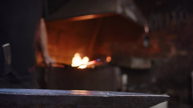 Blacksmith brings hot iron from the forge to the anvil for hammering, smithy