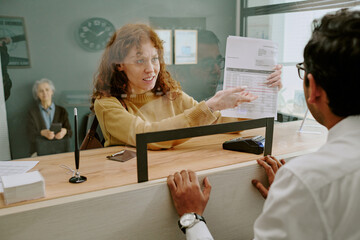 Scene showing woman discussing documents with bank employee at reception counter with senior in...