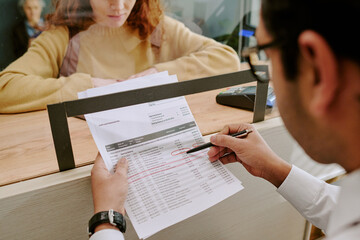 Person at service counter discussing document with client, highlighting essential details using red...
