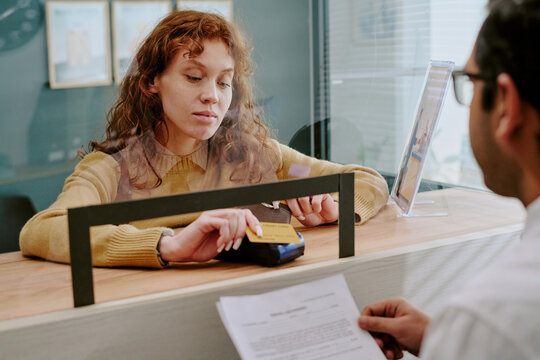 Customer engaging with bank representative while processing financial transaction at service counter with paperwork and credit card reader visible on desk