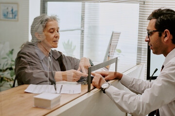 Senior woman engaging professional at counter in office setting, discussing paperwork. Interaction...
