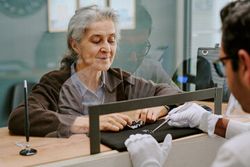 Obraz premium Elderly woman carefully examining pieces of jewelry at counter with jeweler's assistance, reflecting thoughtful consideration