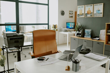 Modern office setup featuring clean desks with organized papers and gadgets, complemented by natural light through large windows, creating an efficient work environment