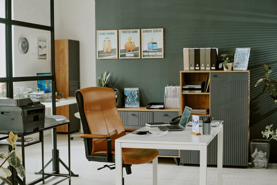 Modern office with organized furniture featuring desk, chair, printer, and storage units, walls decorated with motivational posters, creating a professional environment