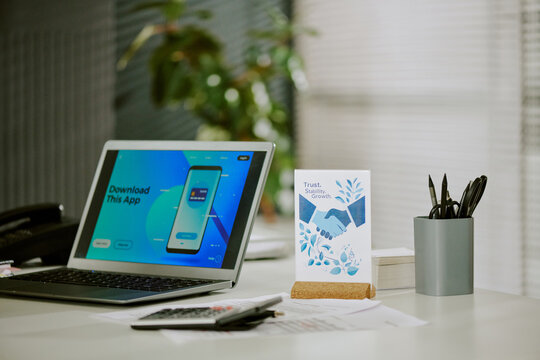 Promoting mobile application download with a laptop displaying app screen placed on desk in modern office environment