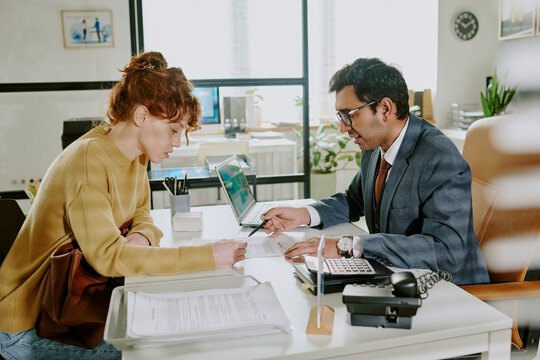 Businesswoman meeting with male professional in modern office environment, discussing documents and sharing polite conversation at desk while both engaged in task