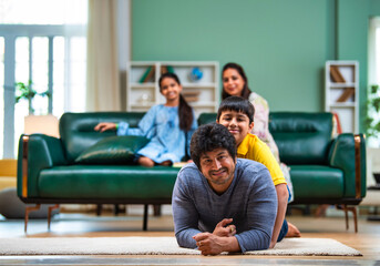 Obraz premium Playful Indian kid rides on dad’s back as he smiles at the camera, with mom and sister watching