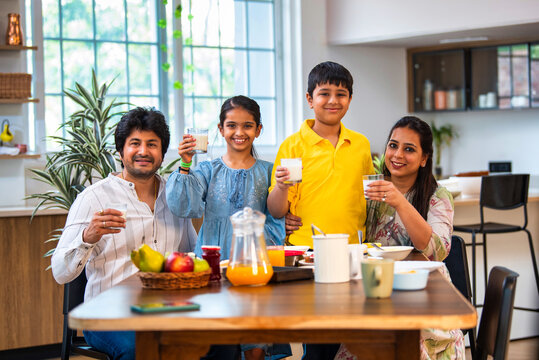 Smiling Indian parents and kids holding milk glasses, promoting a nutritious breakfast at home