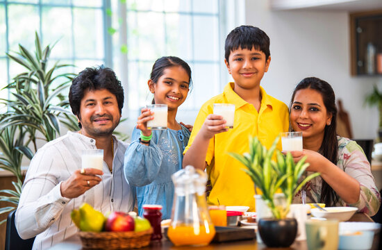 Smiling Indian parents and kids holding milk glasses, promoting a nutritious breakfast at home