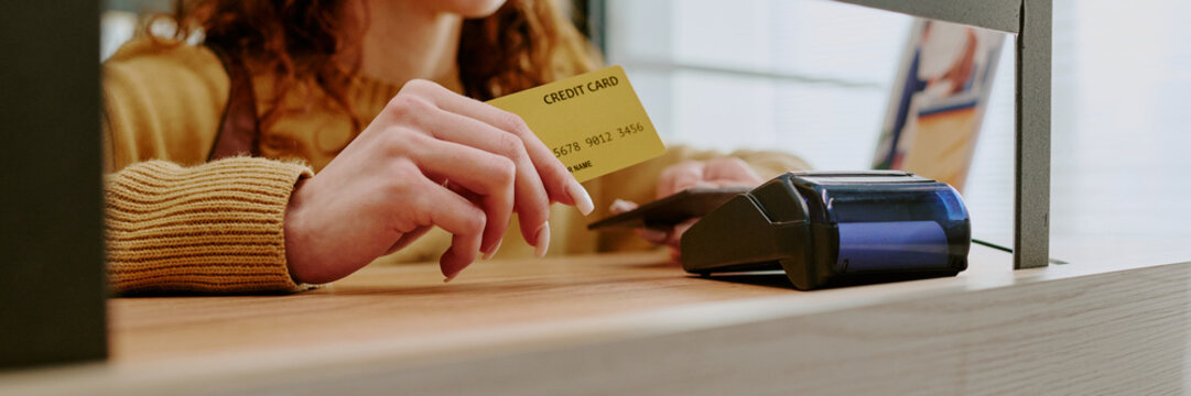 Woman making payment using credit card at retail store checkout counter. Electronic card reader processing transaction captured from close-up view