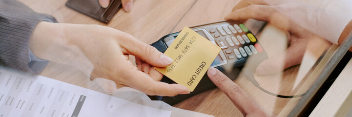 Zoomed-in view of person swiping credit card through payment terminal during transaction in busy retail store environment reflecting hands and device